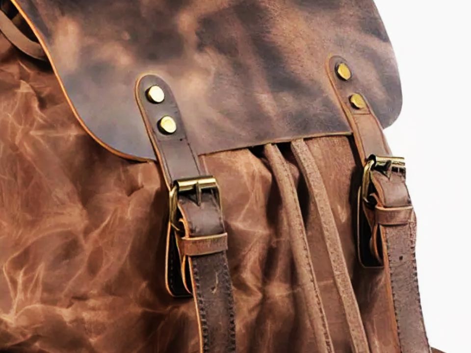 Close-up of the leather flap straps and metal buckles on a waxed canvas backpack