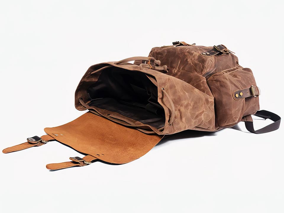 Coffee waxed canvas backpack lying with its leather flap open and main compartment visible