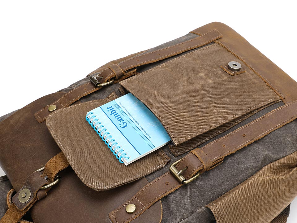 Small notebook tucked into the front pocket of a waxed canvas backpack with the flap open