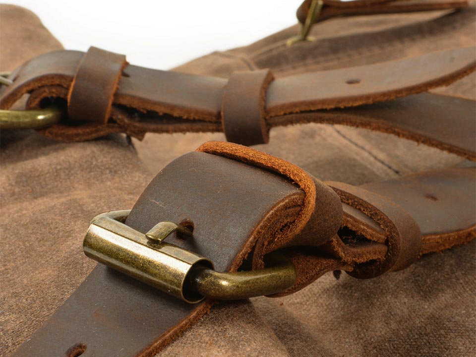 Close-up of the leather fastening strap and metal buckle on a waxed canvas backpack