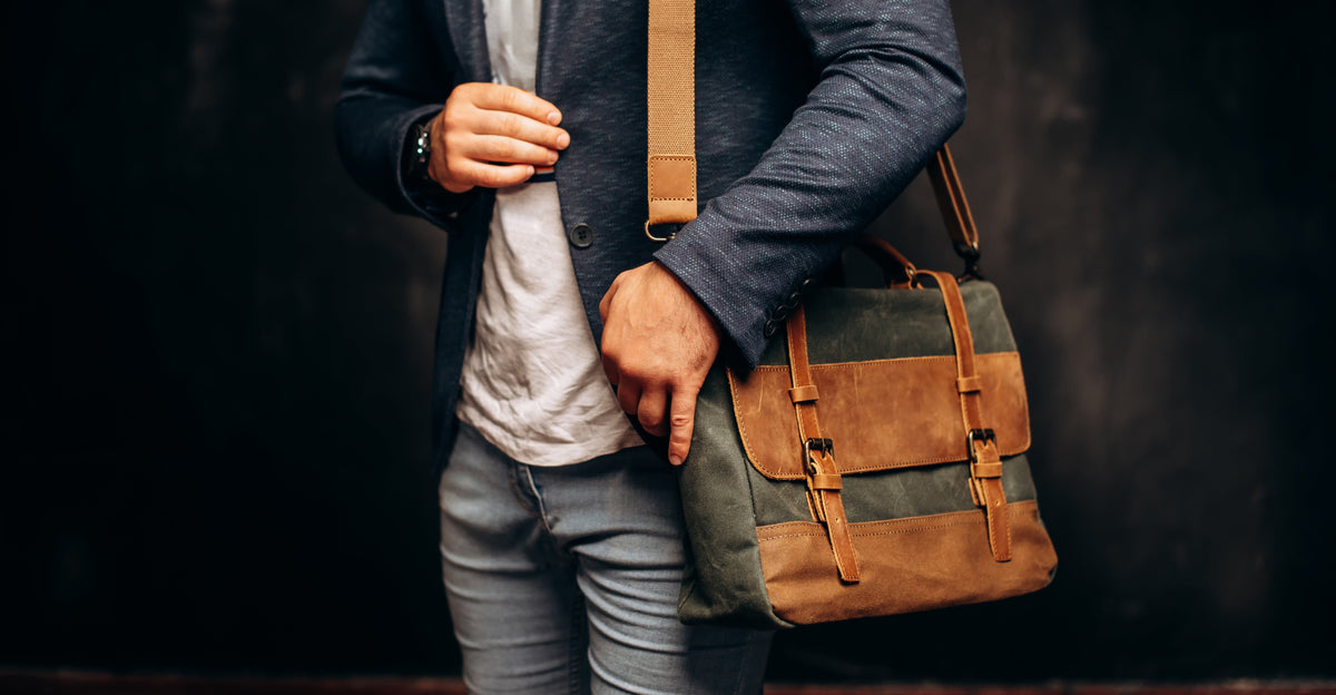 Man carrying a green canvas messenger bag with brown leather trim on his shoulder