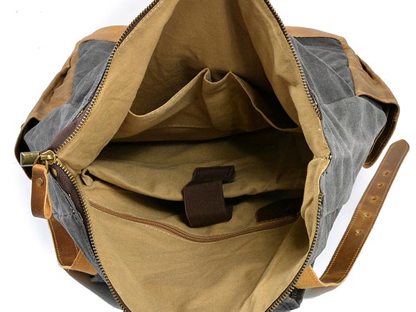 Open waxed canvas backpack showing a padded laptop sleeve, retaining strap and two inner pockets