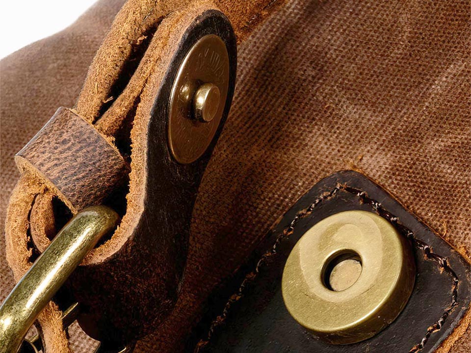 Close-up of the magnetic snap fastening and leather strap on a waxed canvas backpack