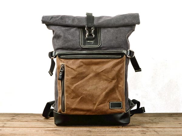 Waxed canvas roll top backpack with a leather front panel standing on a wooden surface