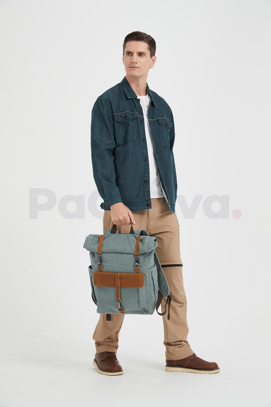 Man holding a blue waxed canvas roll top backpack by its top handle