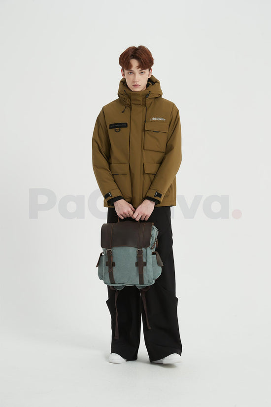 Man holding a blue waxed canvas backpack with a leather flap with both hands in front of him