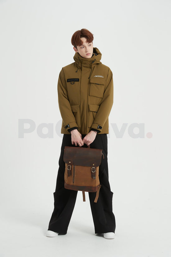 Man holding a khaki waxed canvas backpack with a leather flap with both hands in front of him