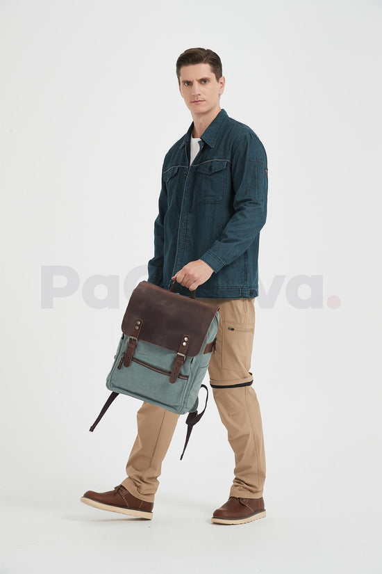 Man mid-step carrying a lake green canvas backpack with a leather flap by its top handle