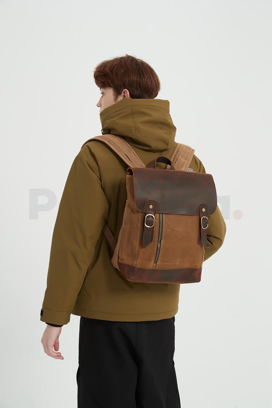 Man wearing a khaki waxed canvas backpack with a leather flap and turning his head toward the left, seen from behind