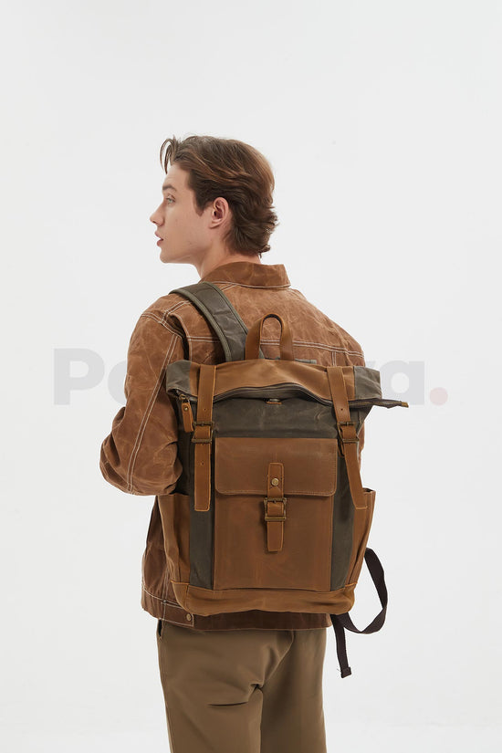 Man wearing a coffee waxed canvas roll top backpack with a leather front pocket and turning his head toward the left, seen from behind