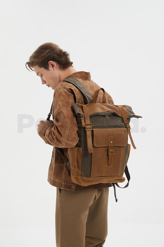 Man wearing a coffee waxed canvas roll top backpack with a leather front pocket, looking down toward the left, seen from behind