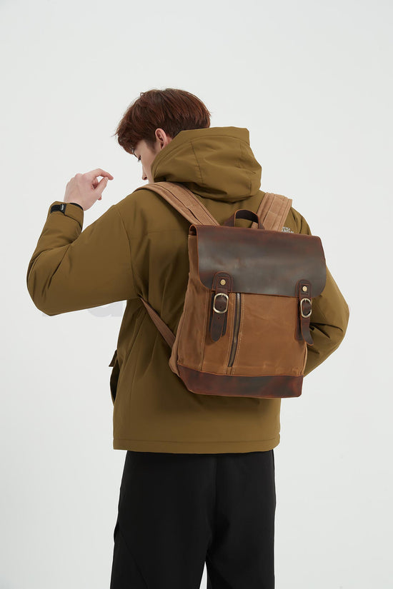 Man wearing a khaki waxed canvas backpack with a leather flap, looking down toward the right, seen from behind