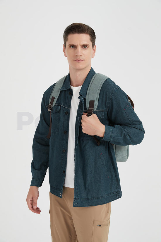 Front view of a man wearing a lake green canvas backpack with a leather flap and holding a shoulder strap