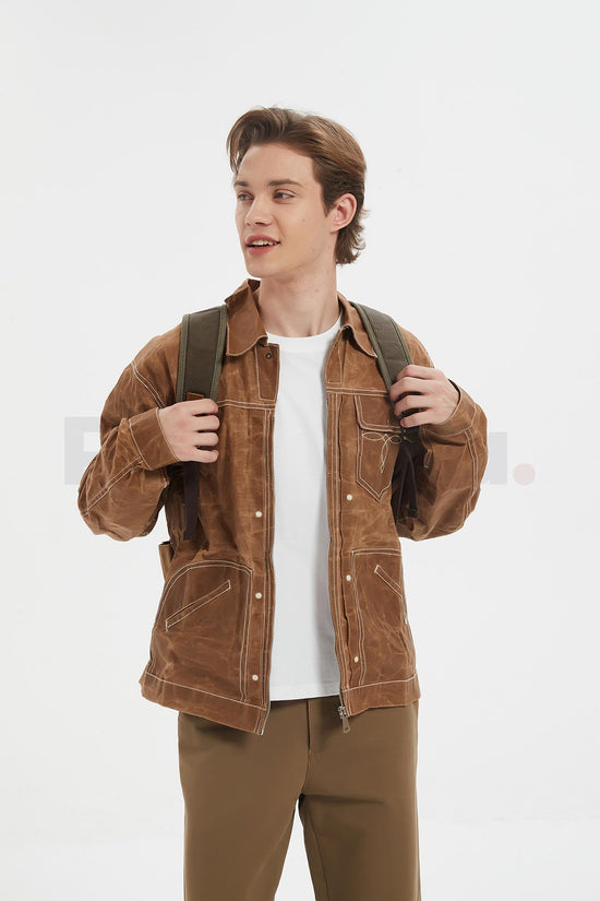 Front view of a man wearing a coffee waxed canvas roll top backpack with a leather front pocket and holding a shoulder strap