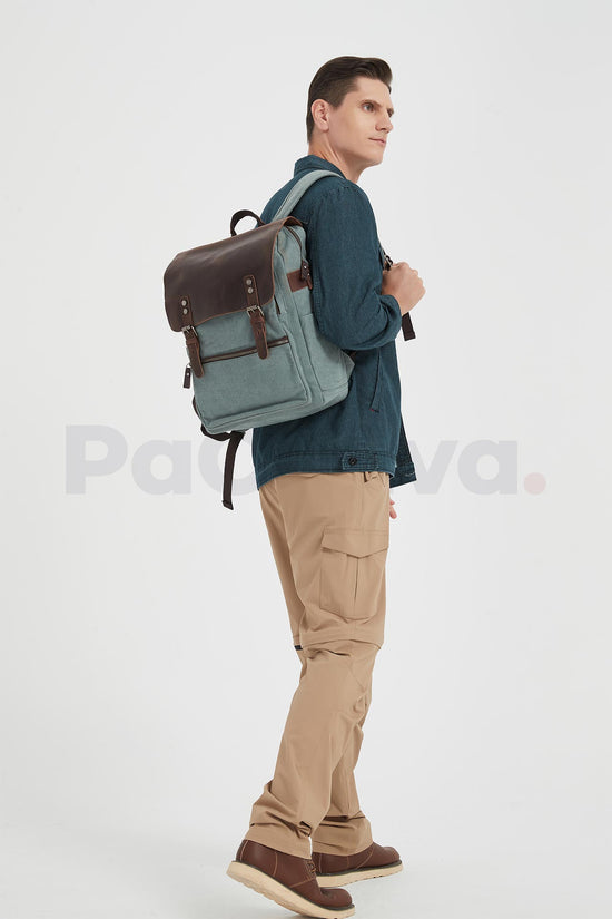 Man facing right while wearing a lake green canvas backpack with a leather flap and holding a shoulder strap, seen from the side