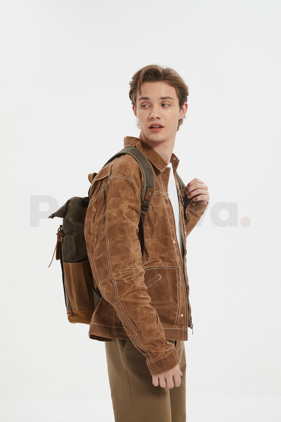 Side view of a man holding a shoulder strap and looking over his shoulder while wearing a coffee waxed canvas roll top backpack
