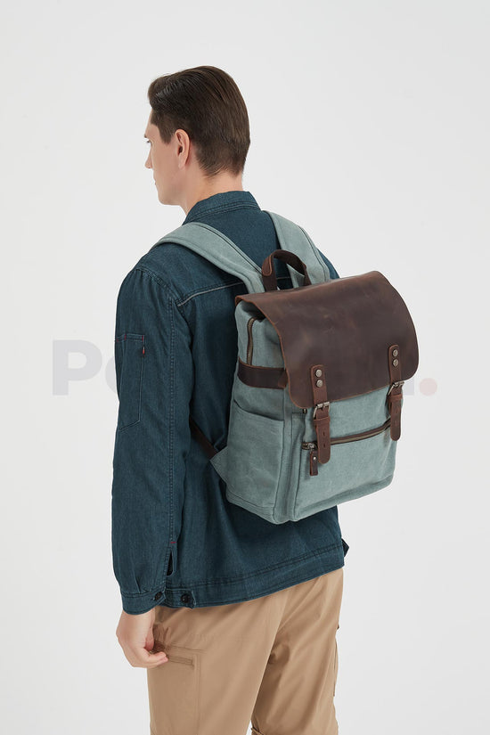 Rear three-quarter view of a man wearing a lake green canvas backpack with a leather flap and facing left
