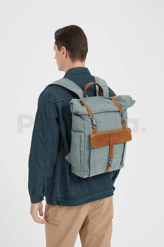 Rear three-quarter view of a man wearing a blue waxed canvas roll top backpack