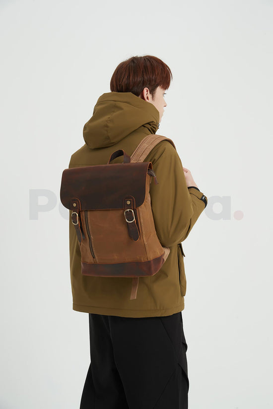 Rear three-quarter view of a man wearing a khaki waxed canvas backpack with a leather flap and facing right