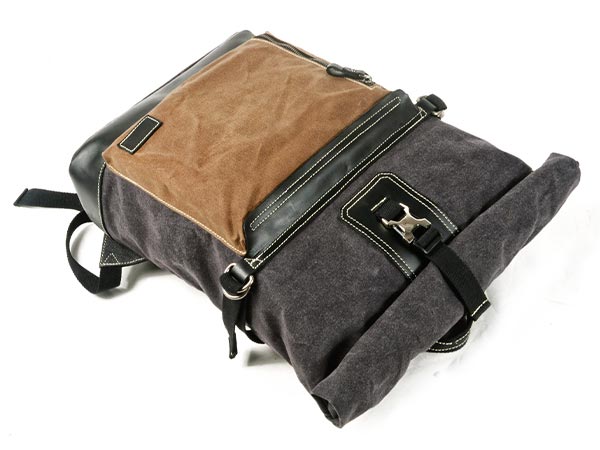 Waxed canvas roll top backpack lying flat with its front zipper pockets visible