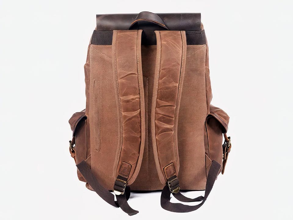Back of a coffee waxed canvas backpack showing padded shoulder straps and a leather carry handle