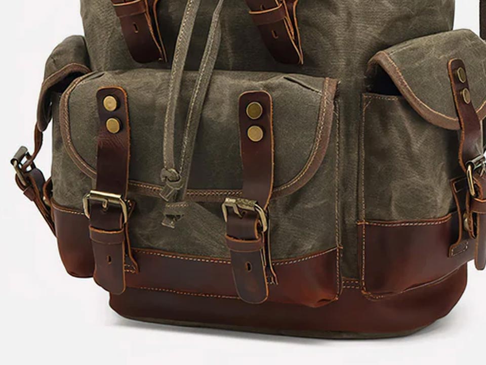 Front flap pocket and leather buckle straps on an army green waxed canvas backpack