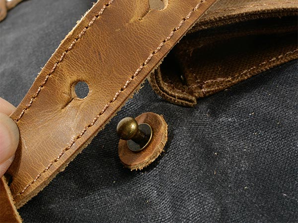 Close-up of a metal fastener and stitched leather strap on a waxed canvas backpack