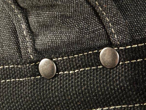 Close-up of metal rivets and reinforced stitching on a waxed canvas backpack