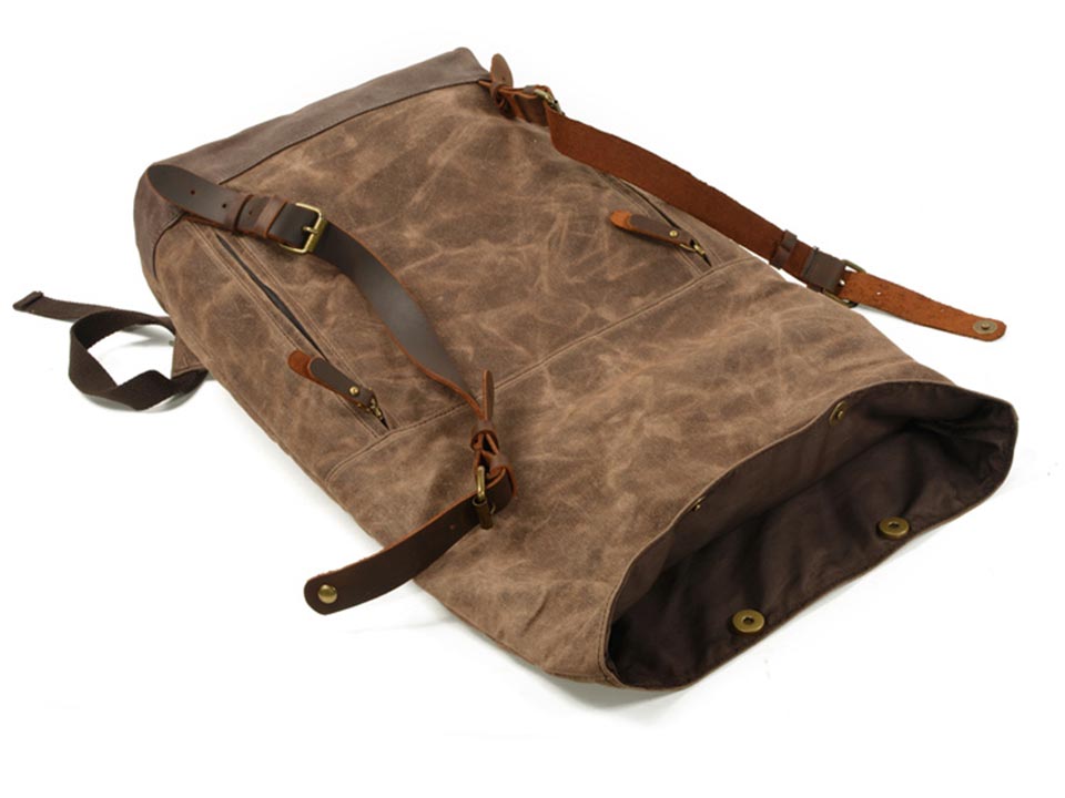 Coffee waxed canvas backpack lying with the roll top open and leather buckle straps extended
