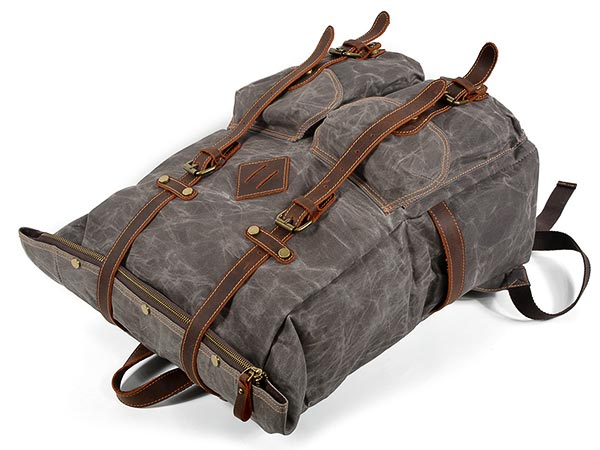 Waxed canvas backpack lying with its roll top extended and leather fastening straps visible