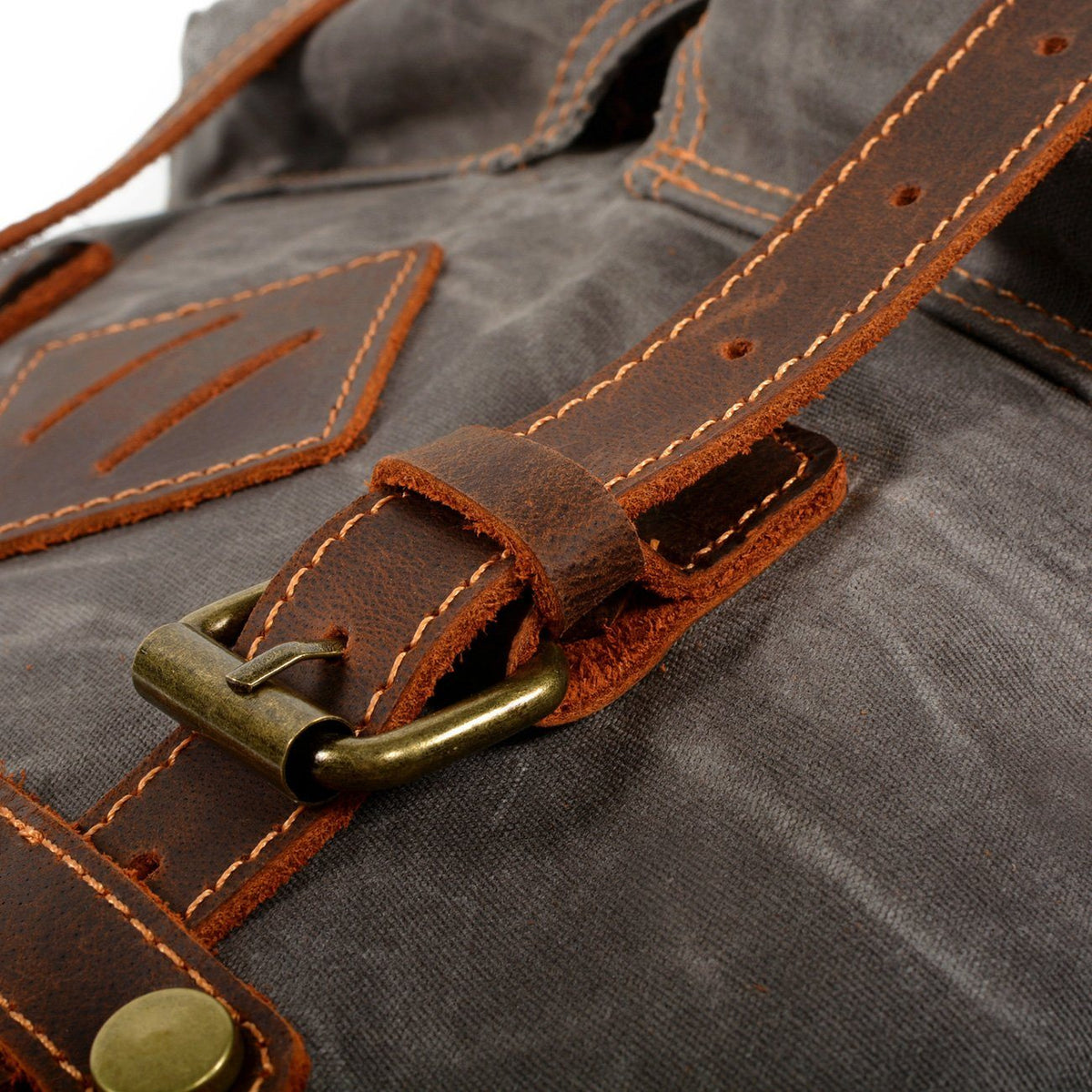 Brass buckle and stitched leather fastening strap on gray waxed canvas backpack.