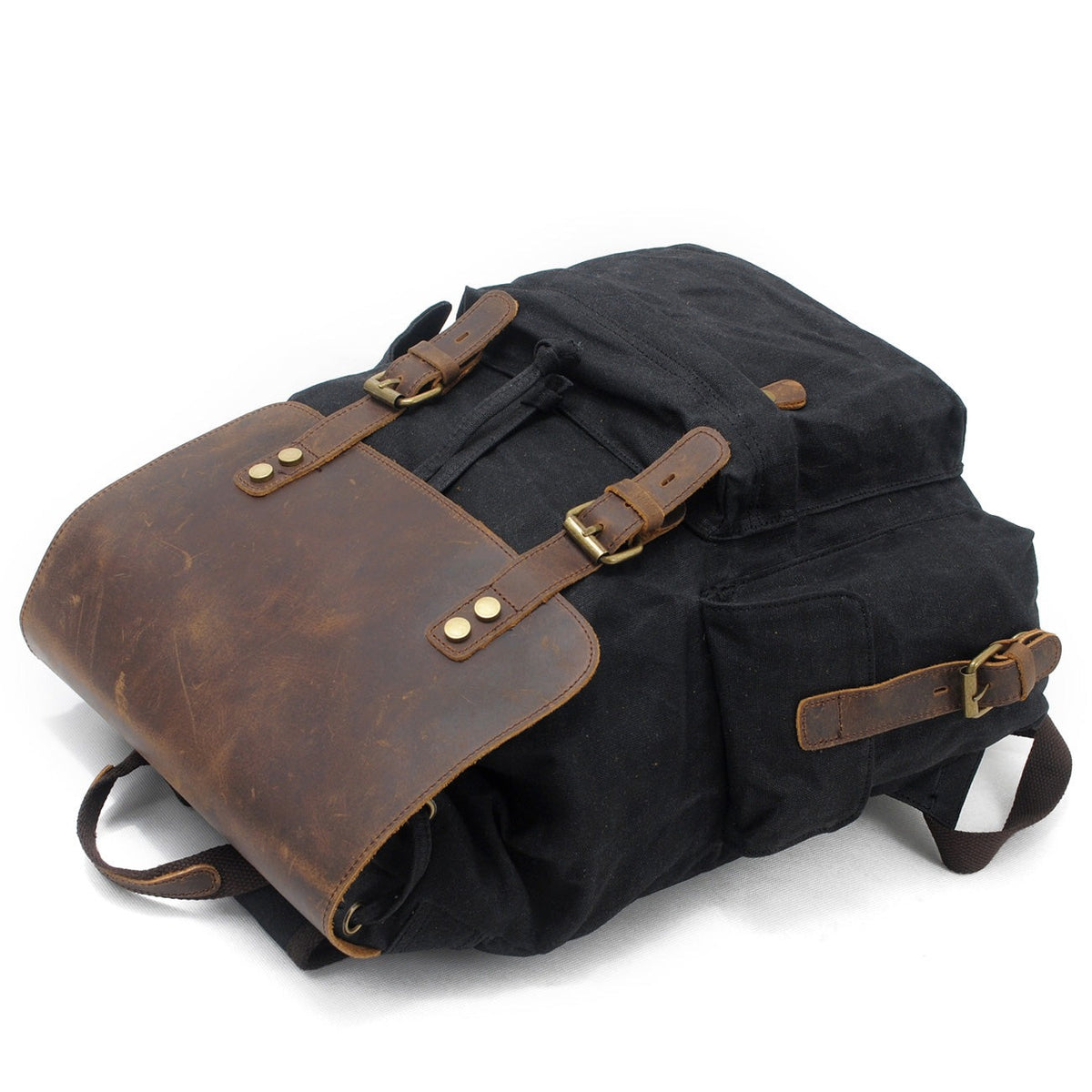 Black waxed canvas backpack lying flat with the flap closed