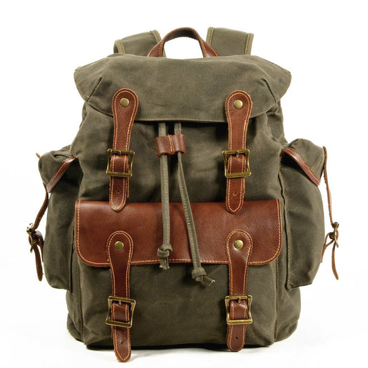 Front of army green waxed canvas backpack with leather-trimmed front pocket and twin buckle straps.