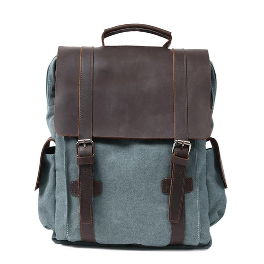 Front of blue waxed canvas backpack with broad leather flap and twin buckle straps.