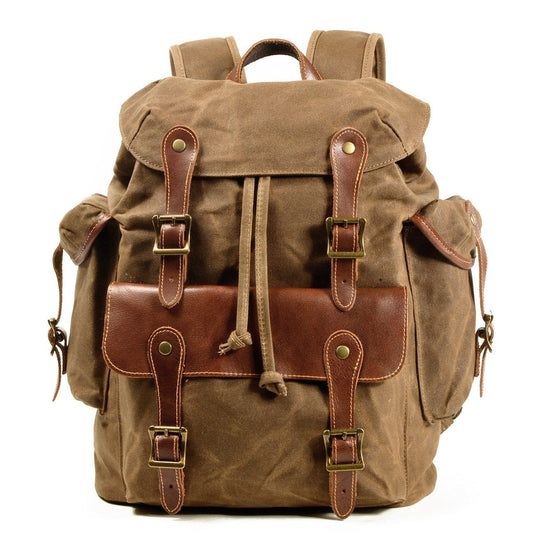 Front of khaki waxed canvas backpack with leather-trimmed front pocket and twin buckle straps.