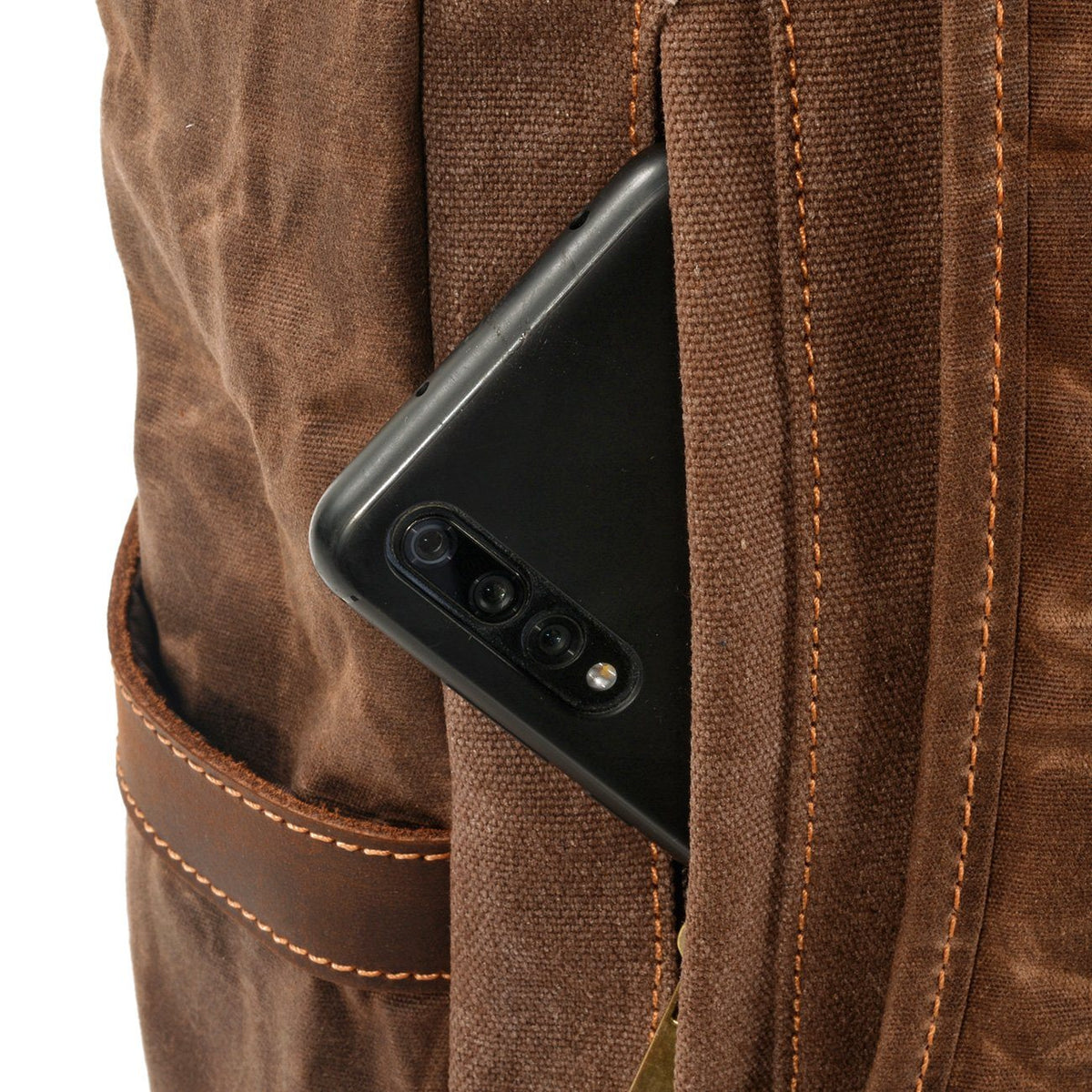 Phone tucked into the hidden back pocket of coffee waxed canvas backpack, beside a padded shoulder strap.