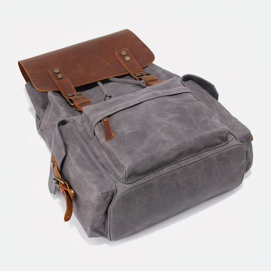 Three-quarter view of the canvas backpack showing its leather flap, front pocket and side pockets