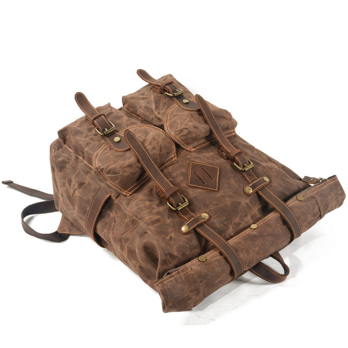 Coffee waxed canvas backpack lying down with twin front pockets, leather buckle straps and carry handles visible.