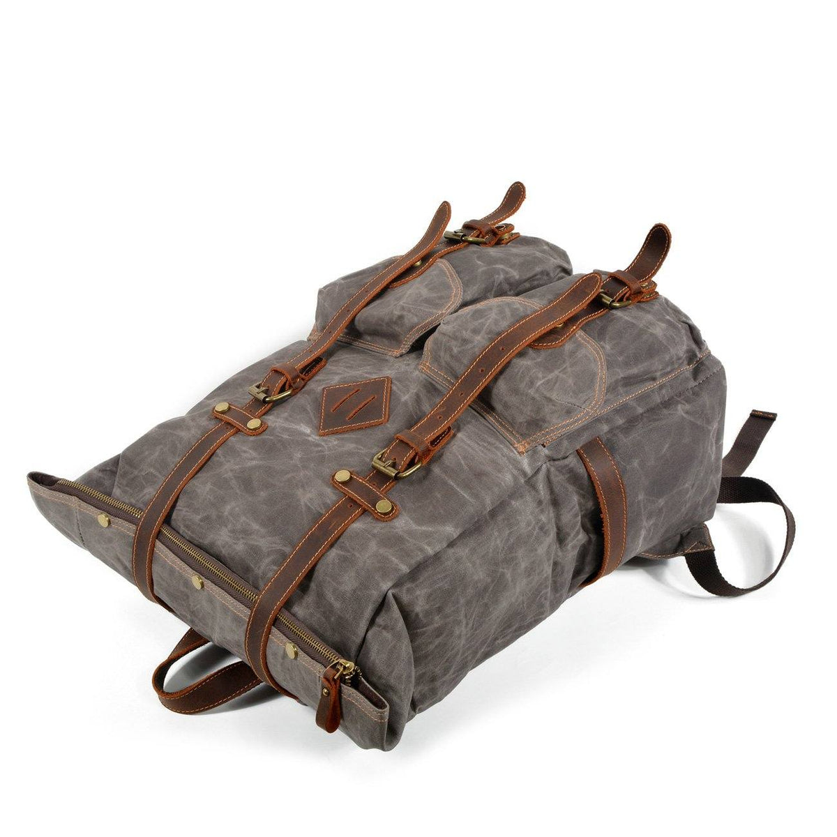 Gray waxed canvas backpack lying on its back with leather buckle straps and front pockets facing upward.