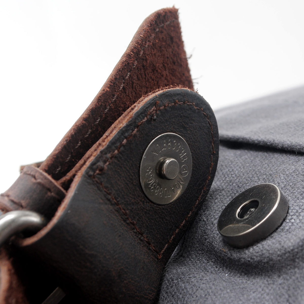 Metal snap on a leather tab of the gray roll top backpack