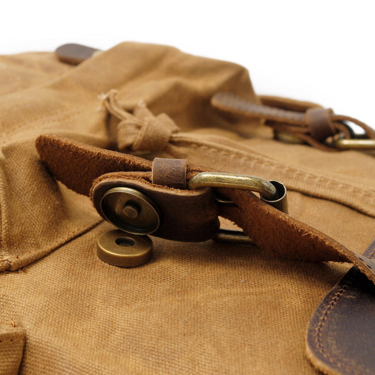 Close-up of the brass magnetic buckle under the khaki backpack flap