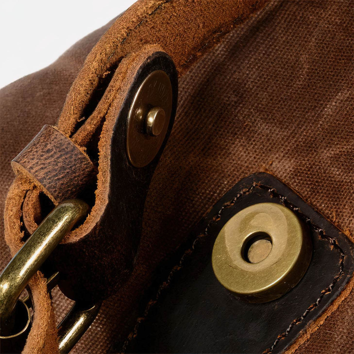 Close-up of the open magnetic snap beneath a leather buckle tab on coffee waxed canvas backpack.