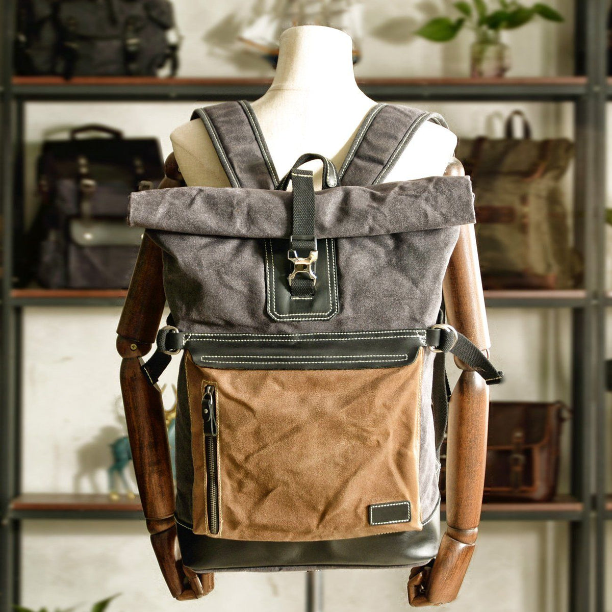 Canvas roll top backpack displayed on a wooden mannequin with its front pocket and buckle visible