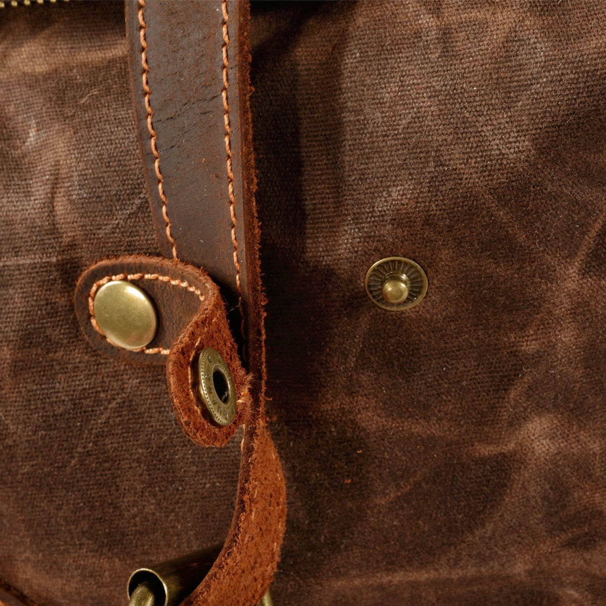 Open snap fastener on a leather tab attached to coffee waxed canvas backpack.