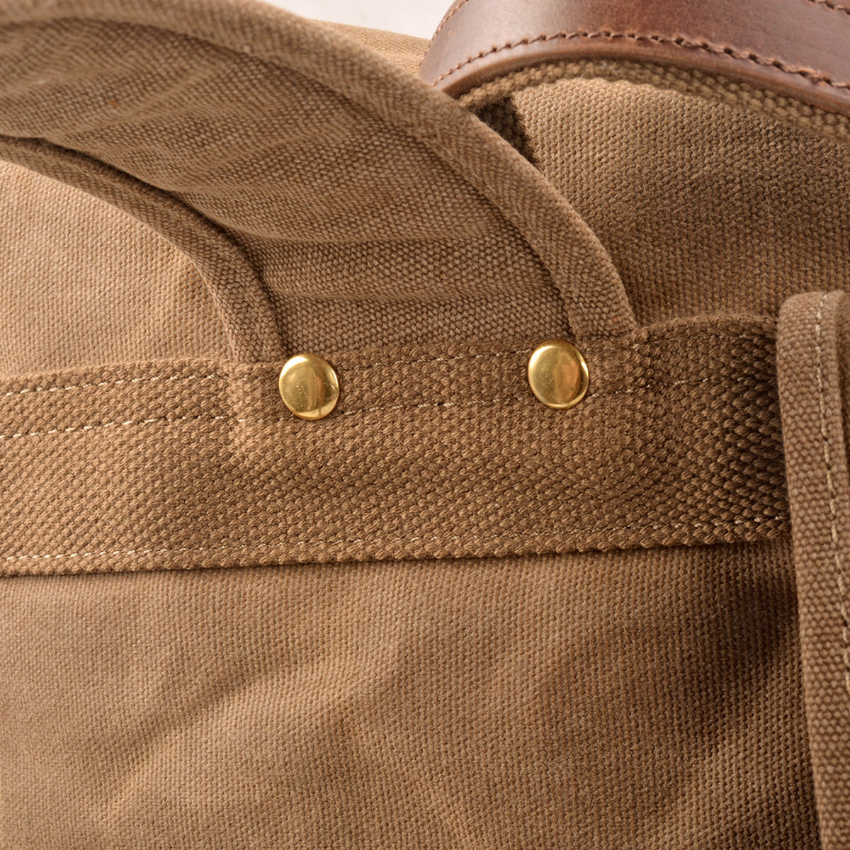 Close-up of brass rivets securing the Khaki backpack's shoulder strap to a woven reinforcement band.
