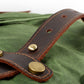 Close-up of a riveted leather strap tab on Army waxed canvas.