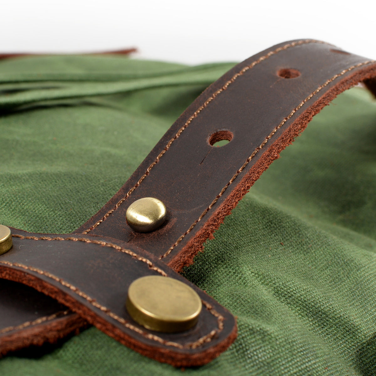Close-up of a riveted leather strap tab on Army waxed canvas.