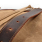 Punched leather strap resting on the khaki canvas flap
