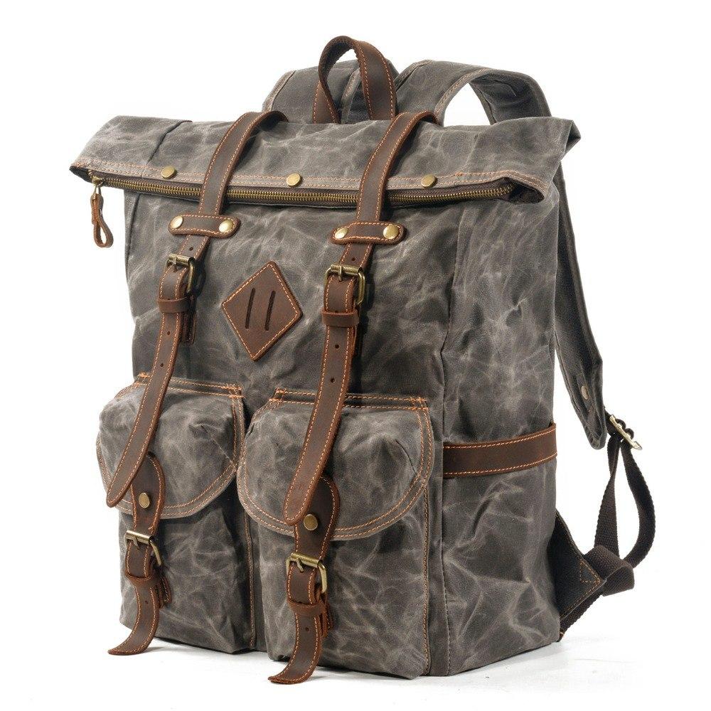 Gray waxed canvas roll top backpack at an angle, showing front flap pockets and side storage.
