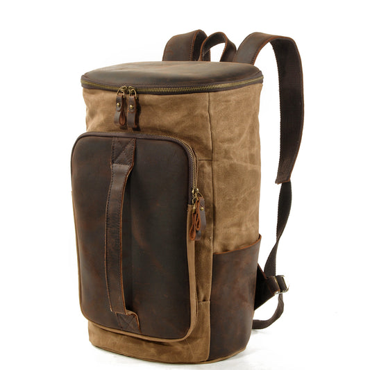 Three-quarter view of the khaki waxed canvas backpack showing the leather grab handle and side slip pocket